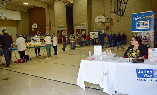 volunteers at tables in a gym pack meals