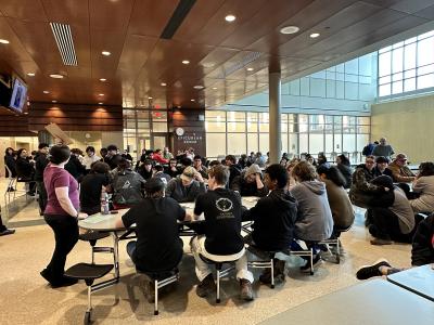 cafeteria full of students listening to a woman give instructions