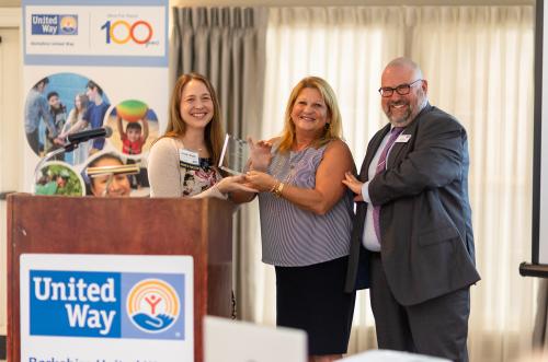 woman hands award to another woman with one man standing next to