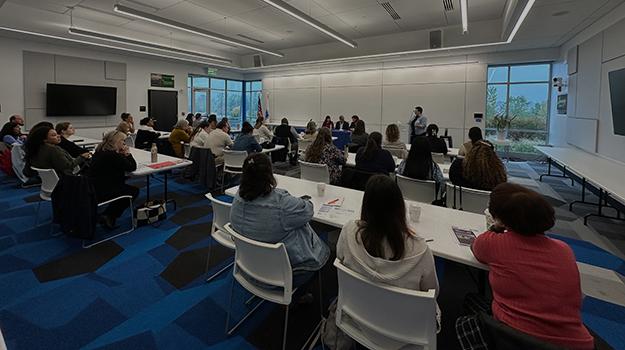 people sit at tables facing a panel of speakers